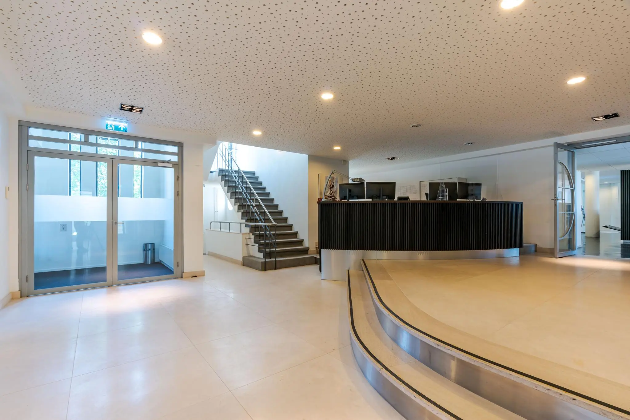 Ingang en receptie van een modern kantoorgebouw aan de Van Alkemadelaan met een trap, balie en glazen deuren.